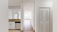 This well-appointed single-floor residence offers a clean, modern aesthetic defined by crisp white walls, abundant natural light, and a cohesive design throughout. The kitchen is a standout feature, showcasing white shaker-style cabinetry, granite countertops, a full suite of stainless steel appliances including a range, microwave, refrigerator, and dishwasher, and light tile flooring. A pass-through counter with pendant lighting connects the kitchen to the adjacent living area, creating an open and social atmosphere. The living space features warm wood-tone flooring and large windows fitted with blinds that allow natural light to pour in, while a ceiling fan adds comfort to the room. A central hallway connects the living areas to the private quarters, with a louvered storage closet providing convenient organization. The bedrooms are finished with plush carpeting and feature windows that bring in soft, natural light. The two bathrooms are tastefully finished with tile flooring, granite-topped white vanities, and chrome hardware. One bathroom offers a tiled soaking tub and shower combination, while the other features a glass-enclosed walk-in shower. Together, these spaces create a bright, functional, and comfortable living environment.