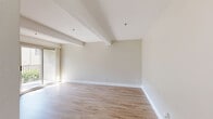 Located at 1375 W San Bernardino Rd in Covina, CA, this one-bedroom, two-bathroom unit offers a thoughtfully designed single-floor layout that maximizes every square foot. Light wood-style flooring runs throughout the main living areas, lending a clean, cohesive aesthetic that brightens the space. The open-concept living room features distinctive exposed ceiling beams that add architectural character, along with a wall-mounted AC unit and a ceiling fan to ensure year-round comfort. Natural light filters in through window blinds, creating a warm and inviting ambiance. The galley-style kitchen is well-appointed with warm-toned wood cabinetry lining both walls, ample counter space, a stainless steel sink, and white gas range and refrigerator — offering efficient functionality in a compact footprint. A hallway connects the living areas to the bedroom and bathrooms, with one bathroom showcasing a wood vanity with a large mirror and generous drawer storage. The second bathroom features a full tub-shower combination with sliding glass doors. The spacious primary bedroom is finished with plush carpet flooring, exposed ceiling beams, and a window that allows natural light to fill the room, creating a comfortable and restful retreat.
