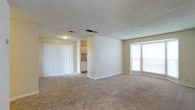 This single-story unit at Fox Run offers a straightforward, functional layout with a neutral color palette of warm beige tones throughout. The living area is generously proportioned, featuring plush wall-to-wall carpeting, a textured ceiling, and large windows fitted with vertical blinds that allow ample natural light. A standout architectural detail is the curved bay window, which adds character to the main living space and enhances the sense of openness.

The kitchen is positioned adjacent to the living area, partially separated by a dividing wall. It includes white cabinetry, laminate countertops with a wood-tone edge, and a stainless steel sink, providing practical storage and workspace.

Multiple carpeted bedrooms are present throughout the unit, each featuring windows with horizontal blinds, white trim, and closet access. The rooms offer comfortable proportions with clean, simple finishes.

Two bathrooms serve the unit. Each includes a white vanity with an integrated sink, a medicine cabinet with mirror, and tile flooring. One bathroom features a full bathtub with a shower curtain rod, while the other offers a dual-mirror vanity configuration, providing added convenience.

Connecting hallways link the rooms cohesively, contributing to a well-organized and accessible floor plan.