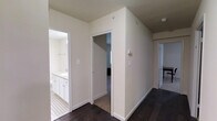 This single-floor residence offers a clean, contemporary aesthetic defined by neutral tones and quality finishes throughout. The interior is anchored by rich, dark hardwood flooring that runs through the main hallway and living areas, providing a striking contrast against the crisp white walls and trim. The hallway serves as the central artery of the home, connecting multiple rooms with an open and airy flow. A well-designed bathroom is accessible directly from the corridor, featuring white cabinetry with ample storage, a vanity with countertop space, and classic tile flooring with a decorative pattern that adds a subtle design detail. The bedroom, visible through an adjoining doorway, continues the dark hardwood flooring and benefits from the home's overall sense of calm and light. White door frames and baseboards provide clean architectural definition throughout, while the neutral wall palette keeps the space feeling bright and versatile. The layout is practical and efficient, with each room thoughtfully positioned for ease of access. Overall, this residence presents a polished, move-in-ready environment with consistent design choices that create a cohesive and inviting atmosphere from room to room.