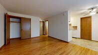 This single-floor unit offers a straightforward and functional layout designed for comfortable everyday living. The main living area is characterized by warm, honey-toned hardwood flooring that extends throughout, creating a cohesive and inviting atmosphere. Large windows along one wall allow natural light to fill the space, further enhancing the open feel of the room. A baseboard heating system runs beneath the windows, providing efficient warmth throughout the colder months.

The kitchen is positioned adjacent to the living area and features white upper and lower cabinetry offering ample storage, a countertop with an integrated sink, and a full suite of white appliances including a coil-top electric range and refrigerator. The kitchen floor transitions to a neutral tile surface, and warm wood-toned paneling adds a classic mid-century character to the space.

The bathroom is finished with full white subway tile surrounding a standard soaking bathtub and shower combination, complemented by chrome fixtures. A pink mosaic tile floor adds a charming vintage detail. Interior doors throughout the unit are solid wood with warm stained finishes, consistent with the overall classic aesthetic. The unit presents a clean, understated design that provides a solid foundation for personalization.