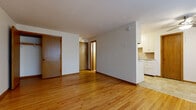 This single-floor unit offers a straightforward and functional layout designed for comfortable everyday living. The main living area is characterized by warm, honey-toned hardwood flooring that extends throughout, creating a cohesive and inviting atmosphere. Large windows along one wall allow natural light to fill the space, further enhancing the open feel of the room. A baseboard heating system runs beneath the windows, providing efficient warmth throughout the colder months.

The kitchen is positioned adjacent to the living area and features white upper and lower cabinetry offering ample storage, a countertop with an integrated sink, and a full suite of white appliances including a coil-top electric range and refrigerator. The kitchen floor transitions to a neutral tile surface, and warm wood-toned paneling adds a classic mid-century character to the space.

The bathroom is finished with full white subway tile surrounding a standard soaking bathtub and shower combination, complemented by chrome fixtures. A pink mosaic tile floor adds a charming vintage detail. Interior doors throughout the unit are solid wood with warm stained finishes, consistent with the overall classic aesthetic. The unit presents a clean, understated design that provides a solid foundation for personalization.
