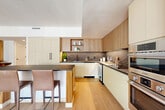 Located in the heart of Washington, DC, Unit 1214 at 1425 New York Ave NW is a thoughtfully designed one-bedroom, three-bathroom residence offering generous living space across a single open floor. Light oak hardwood flooring flows throughout, tying together a cohesive, modern aesthetic. The chef's kitchen is a standout feature, showcasing custom cabinetry in warm wood and matte cream tones, a dramatic dark marble backsplash, and a distinctive oval-shaped island with fluted wood detailing and a dark countertop — ideal for casual dining or entertaining. The living area is bright and airy, with large windows allowing ample natural light, while the adjacent dining room opens directly to a private balcony with city views through floor-to-ceiling sliding glass doors. The spacious primary bedroom enjoys its own balcony access and large windows framing urban views. Three full bathrooms feature clean, contemporary finishes including large-format stone tile, warm wood vanities, and black hardware accents. A dedicated laundry room with side-by-side washer and dryer adds convenience, while four closets — including a generously sized walk-in — provide ample storage throughout.