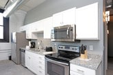 This single-floor loft-style space masterfully combines industrial heritage with modern comfort. The open layout is anchored by striking exposed white-painted brick walls and soaring ceilings with visible ductwork and track lighting, reflecting the building's historic character throughout.

The kitchen is well-appointed with white shaker cabinetry, granite countertops, and a full suite of stainless steel appliances including a range, dishwasher, microwave, and refrigerator, all set against polished concrete flooring. Black-framed windows throughout the space flood each room with natural light while offering urban views.

The living area features the same exposed brick backdrop, creating a warm, loft-like ambiance ideal for relaxing or entertaining. Two bedrooms are present: one showcases the original brick walls and benefits from natural light through a black-trimmed window, while the second features smooth painted walls, wall sconce lighting, and a double-door closet. Both rooms are comfortably appointed.

A full bathroom with tile flooring, a single-sink vanity, and a shower-tub combination completes the layout. The consistent industrial aesthetic, marked by concrete floors, exposed infrastructure, and historic masonry, gives this space a distinctive and cohesive character.