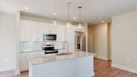 Located at 4521 Landmark Dr in Raleigh, NC, this single-floor residence offers a thoughtfully designed open-concept layout with modern finishes throughout. The kitchen serves as the centerpiece of the home, featuring a large granite-topped island with an undermount sink, white shaker-style cabinetry, a subway tile backsplash, and a full suite of stainless steel appliances including a range, microwave, and French door refrigerator. Three globe pendant lights hang above the island, adding a stylish touch to the space. Wood-look plank flooring extends through the main living areas, complementing the neutral warm-toned walls and crisp white trim. The living area is bright and open, benefiting from multiple windows that invite natural light and views of the surrounding greenery. A private balcony is accessible directly from the kitchen area. The bedrooms are carpeted for comfort and include ceiling fans and windows for ventilation and light. The primary bathroom is well-appointed with granite countertops, white cabinetry, a frameless glass shower, and access to a walk-in closet with built-in shelving. An additional bathroom features a soaking tub with subway tile surround and brushed nickel fixtures, rounding out this clean and contemporary residence.