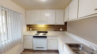 Located at 2841 E Lincoln Ave in Anaheim, California, this single-floor unit offers a practical and clean layout with a variety of updated finishes throughout. The kitchen is well-appointed with white upper and lower cabinetry providing ample storage, light-toned quartz-style countertops, a wood-look tile backsplash, and a gas range. Light wood-style flooring runs through the kitchen and extends into the main living areas, creating a cohesive and easy-to-maintain surface. The living room is a comfortable, open space featuring a ceiling fan with light fixture and a large picture window that allows natural light to fill the room, offering views of the surrounding greenery. An additional room, also with wood-style flooring, includes a wall-mounted air conditioning unit and a window with vertical blinds. The bedroom is carpeted and features sliding mirrored closet doors that add depth to the room, along with a textured ceiling. The bathroom includes a full-size soaking tub and shower combination with chrome fixtures set against clean white surroundings. Throughout the unit, textured ceilings and neutral wall tones provide a simple, functional aesthetic suited for everyday living.