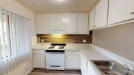 Located at 2841 E Lincoln Ave in Anaheim, California, this single-floor unit offers a practical and clean layout with a variety of updated finishes throughout. The kitchen is well-appointed with white upper and lower cabinetry providing ample storage, light-toned quartz-style countertops, a wood-look tile backsplash, and a gas range. Light wood-style flooring runs through the kitchen and extends into the main living areas, creating a cohesive and easy-to-maintain surface. The living room is a comfortable, open space featuring a ceiling fan with light fixture and a large picture window that allows natural light to fill the room, offering views of the surrounding greenery. An additional room, also with wood-style flooring, includes a wall-mounted air conditioning unit and a window with vertical blinds. The bedroom is carpeted and features sliding mirrored closet doors that add depth to the room, along with a textured ceiling. The bathroom includes a full-size soaking tub and shower combination with chrome fixtures set against clean white surroundings. Throughout the unit, textured ceilings and neutral wall tones provide a simple, functional aesthetic suited for everyday living.