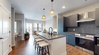 Located at 21 West 2nd Avenue in Columbus, Ohio, this well-appointed one-bedroom, one-bathroom residence offers a thoughtfully designed open-concept layout with modern finishes throughout. Warm hardwood flooring flows seamlessly through the main living areas, anchoring the space with a cohesive, contemporary aesthetic.

The kitchen and living room share an open, connected footprint, centering around a large kitchen island with a dark quartz countertop and bar seating for three, illuminated by a pair of woven pendant lights. The kitchen features matte slate-toned cabinetry, a tile backsplash, stainless steel appliances including a range with a wall-mounted hood, and a full-size refrigerator. The living area benefits from large floor-to-ceiling windows and a glass door that opens directly onto a private balcony, filling the space with natural light and offering views of the surrounding neighborhood.

The bedroom is a comfortable retreat with plush carpeting, soft neutral walls, a large window with outdoor views, and a dedicated closet. The bathroom is finished with large-format stone-look tile flooring, dark modern cabinetry with an integrated vanity, and a glass-enclosed walk-in shower. Clean white panel doors with matte black hardware appear throughout, adding a refined, consistent design touch to the entire unit.