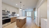 This thoughtfully designed one-bedroom, one-bathroom residence in Dallas, Texas offers a modern open-concept layout with stylish finishes throughout. The combined kitchen and living area serves as the heart of the home, featuring light hardwood-style flooring, recessed lighting, and a ceiling fan. The kitchen is well-appointed with two-tone cabinetry — upper white cabinets paired with warm wood lower cabinets — white quartz countertops, a textured geometric tile backsplash, stainless steel appliances including a refrigerator, range, and microwave, and a central island with pendant lighting that doubles as a breakfast bar. The living area flows naturally from the kitchen and receives natural light through French doors. The spacious bedroom is carpeted, includes a ceiling fan, and connects to a walk-in closet with wire shelving for organized storage. The full bathroom features a wood-tone vanity with a wide mirror, white countertop, soaking tub with tile surround, and light tile flooring. A dedicated laundry area houses a full-sized washer and dryer. Clean lines, neutral tones, and quality materials give this residence a cohesive, contemporary feel throughout.