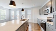 Located at 2223 Lee Rd in Cleveland Heights, OH, this well-appointed 2-bedroom, 2-bathroom single-floor residence offers a thoughtfully designed layout with modern finishes throughout. The open-concept kitchen and living area serves as the heart of the home, featuring a large central island with a quartz countertop, undermount sink, and stylish pendant lighting. Gray shaker-style cabinetry, a white tile backsplash, stainless steel appliances—including a range and over-the-range microwave—and rich hardwood-style flooring complete the kitchen's contemporary aesthetic. The living room is bathed in natural light from multiple large windows fitted with horizontal blinds, and continues the warm hardwood-style flooring. A clean, well-lit hallway connects the main living spaces to the private quarters. Both bedrooms feature plush carpet flooring and generous windows that invite natural light. The primary bedroom is a comfortable retreat with a dedicated closet offering built-in shelving and hanging rods. The bathrooms are finished with gray vanity cabinetry, white quartz countertops, and a tub-shower combination. The overall ambiance is clean, bright, and modern, ideal for contemporary living.