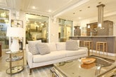Located at 130 Brooke Ave in Norfolk, Virginia, this sophisticated single-floor amenity space blends classic architectural detail with contemporary interior design. Polished terrazzo floors extend throughout, reflecting light and lending a refined, upscale character to every area.

The open-plan kitchen is outfitted with high-end stainless steel appliances, including a professional-grade refrigerator, dark shaker-style cabinetry, white quartz countertops, and a large island with bar seating for multiple guests. Pendant lighting and a statement range hood add both function and style to this well-appointed culinary area.

Adjacent to the kitchen, the main lounge is expansive and bathed in natural light from a series of tall, grid-paned windows along the perimeter. The space is furnished with elegant seating arrangements, including plush sectional sofas, velvet accent chairs in warm gold tones, and curated artwork, including a large-scale abstract canvas that serves as a focal point. A classic fireplace with a detailed mantel anchors one end of the room, while a wall-mounted television adds a modern touch overhead.

A dedicated games area features a full-size billiards table, and a chandelier provides warm ambient lighting. Wainscoting, coffered ceiling details, and decorative moldings throughout the space reinforce its timeless, upscale aesthetic, making it well-suited for both social gatherings and relaxed everyday use.