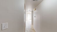 This single-floor residential unit offers a practical and well-organized layout designed for comfortable everyday living. The interior is finished throughout with neutral tones and light-colored walls, creating a clean and cohesive aesthetic across all rooms.

The hallway serves as the central connector of the unit, finished with plush carpeting underfoot and ceiling-mounted lighting that guides movement between spaces. A thermostat and wall-mounted fixtures are conveniently positioned along the corridor.

The kitchen is equipped with warm wood-toned cabinetry that extends to the upper and lower levels, providing ample storage. A white electric range with an overhead vent, a black dishwasher, and a double-basin sink with a countertop workspace complete the functional setup. Light ceramic tile flooring adds durability to the space.

The living and bedroom areas are carpeted and bathed in natural light, thanks to large windows dressed with vertical blinds. The rooms are generously proportioned, with clean walls, standard electrical outlets, and floor vents for climate control.

The bathroom features a wide vanity with an undermount sink, wood-toned cabinetry below, a large wall mirror, a toilet, and a shower enclosure with sliding glass doors. A multi-bulb overhead light fixture provides ample illumination. The overall ambiance of the unit is bright, functional, and move-in ready.