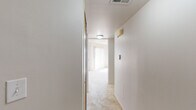 This single-floor residential unit offers a practical and well-organized layout designed for comfortable everyday living. The interior is finished throughout with neutral tones and light-colored walls, creating a clean and cohesive aesthetic across all rooms.

The hallway serves as the central connector of the unit, finished with plush carpeting underfoot and ceiling-mounted lighting that guides movement between spaces. A thermostat and wall-mounted fixtures are conveniently positioned along the corridor.

The kitchen is equipped with warm wood-toned cabinetry that extends to the upper and lower levels, providing ample storage. A white electric range with an overhead vent, a black dishwasher, and a double-basin sink with a countertop workspace complete the functional setup. Light ceramic tile flooring adds durability to the space.

The living and bedroom areas are carpeted and bathed in natural light, thanks to large windows dressed with vertical blinds. The rooms are generously proportioned, with clean walls, standard electrical outlets, and floor vents for climate control.

The bathroom features a wide vanity with an undermount sink, wood-toned cabinetry below, a large wall mirror, a toilet, and a shower enclosure with sliding glass doors. A multi-bulb overhead light fixture provides ample illumination. The overall ambiance of the unit is bright, functional, and move-in ready.