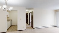 Located at 6941 Collingwood Ln in Woodbury, Minnesota, this single-floor unit offers a practical and well-maintained layout suited for comfortable everyday living. The living and dining areas are finished with neutral-toned carpeting and cream-colored walls, creating a bright and clean atmosphere throughout. Baseboard heating runs along the perimeter of the main living spaces, and a wall-mounted air conditioning unit provides additional climate control. A chandelier fixture highlights the dining area, which connects openly to the kitchen. The kitchen is equipped with white cabinetry, granite-style laminate countertops, a double-basin stainless steel sink, an electric range with overhead ventilation, and a stainless steel dishwasher, all set atop wood-look flooring. A hallway lined with dark-toned doors leads to the private areas of the unit, including multiple rooms with carpeted floors and generous wall space. The bathroom is thoughtfully finished with large-format stone-look tile on both the floor and tub surround, complemented by a white vanity with marble-style countertop and brushed nickel hardware. The overall aesthetic is clean and neutral, offering a move-in ready canvas throughout.