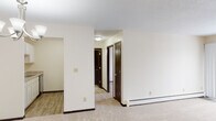 Located at 6941 Collingwood Ln in Woodbury, Minnesota, this single-floor unit offers a practical and well-maintained layout suited for comfortable everyday living. The living and dining areas are finished with neutral-toned carpeting and cream-colored walls, creating a bright and clean atmosphere throughout. Baseboard heating runs along the perimeter of the main living spaces, and a wall-mounted air conditioning unit provides additional climate control. A chandelier fixture highlights the dining area, which connects openly to the kitchen. The kitchen is equipped with white cabinetry, granite-style laminate countertops, a double-basin stainless steel sink, an electric range with overhead ventilation, and a stainless steel dishwasher, all set atop wood-look flooring. A hallway lined with dark-toned doors leads to the private areas of the unit, including multiple rooms with carpeted floors and generous wall space. The bathroom is thoughtfully finished with large-format stone-look tile on both the floor and tub surround, complemented by a white vanity with marble-style countertop and brushed nickel hardware. The overall aesthetic is clean and neutral, offering a move-in ready canvas throughout.