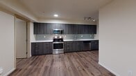 Located at 5246 Brooklyn Ave NE in Seattle's University District, this 2-bedroom, 1-bathroom unit offers a well-designed single-floor layout that maximizes functionality. The open kitchen and living area serves as the heart of the unit, featuring a sleek galley-style kitchen outfitted with dark wood cabinetry, quartz countertops, a mosaic tile backsplash, and a full suite of stainless steel appliances including a refrigerator, range, microwave, and dishwasher. Track lighting illuminates the kitchen and living space, while durable hardwood-style flooring runs throughout the unit, adding warmth and continuity. Two bedrooms provide comfortable accommodations, each with closet space and windows that bring in natural light. The bedrooms are finished with neutral tones and the same hardwood-style flooring. The bathroom is shared with the laundry area, which includes a stacked washer and dryer unit — a convenient in-unit amenity. The bathroom features a vanity with quartz countertop and dark cabinetry consistent with the kitchen's design language. Three closets throughout the unit offer ample storage. A hallway connects the main living areas to the bedrooms, providing a practical and organized flow throughout the space.