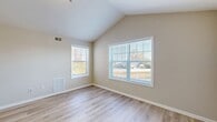 This well-maintained single-floor residence offers a bright and airy atmosphere throughout, highlighted by striking vaulted ceilings that lend a sense of openness and volume to the living areas. Light-toned hardwood flooring runs consistently across the main rooms, providing a clean, cohesive aesthetic that complements the neutral warm-beige wall palette.

The spacious living areas benefit from an abundance of natural light streaming through multiple double-hung windows fitted with horizontal blinds, offering pleasant outdoor views of the surrounding neighborhood. The vaulted ceiling design is a standout architectural feature, rising to a peak and adding character to the open rooms.

The kitchen is equipped with warm wood-toned cabinetry offering generous storage, a kitchen peninsula with counter seating, and a full suite of white appliances including a refrigerator, dishwasher, electric range with over-the-range microwave, all set atop tile flooring. The bathroom features tile flooring, a vanity with storage, and a clean, functional layout.

The bedrooms are generously proportioned, with vaulted or elevated ceilings, large windows allowing ample daylight, and at least one room featuring a closet with built-in shelving. HVAC vents are present throughout, ensuring year-round climate control. The overall layout, as seen in the dollhouse view, is practical and well-organized.