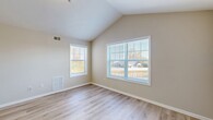 This well-maintained single-floor residence offers a bright and airy atmosphere throughout, highlighted by striking vaulted ceilings that lend a sense of openness and volume to the living areas. Light-toned hardwood flooring runs consistently across the main rooms, providing a clean, cohesive aesthetic that complements the neutral warm-beige wall palette.

The spacious living areas benefit from an abundance of natural light streaming through multiple double-hung windows fitted with horizontal blinds, offering pleasant outdoor views of the surrounding neighborhood. The vaulted ceiling design is a standout architectural feature, rising to a peak and adding character to the open rooms.

The kitchen is equipped with warm wood-toned cabinetry offering generous storage, a kitchen peninsula with counter seating, and a full suite of white appliances including a refrigerator, dishwasher, electric range with over-the-range microwave, all set atop tile flooring. The bathroom features tile flooring, a vanity with storage, and a clean, functional layout.

The bedrooms are generously proportioned, with vaulted or elevated ceilings, large windows allowing ample daylight, and at least one room featuring a closet with built-in shelving. HVAC vents are present throughout, ensuring year-round climate control. The overall layout, as seen in the dollhouse view, is practical and well-organized.
