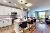 Located at 101 W Morehead St in Charlotte, NC, this contemporary single-floor residence offers a thoughtfully designed open-concept layout that seamlessly connects the living, dining, and kitchen areas. The living room is bright and inviting, featuring hardwood-style flooring, large windows that allow natural light to fill the space, and room for stylish furnishings.

The kitchen is a standout feature, showcasing crisp white shaker cabinetry, light quartz countertops, a subway tile backsplash, and a full suite of stainless steel appliances including a French door refrigerator. A central island with an undermount sink and seating provides an ideal space for casual dining, illuminated by striking pendant lights with gold interiors. A built-in shelving and mudroom area adds functional storage near the entry.

The primary bedroom is spacious and serene, with plush carpeting, a ceiling fan, and direct access to a well-appointed en-suite bathroom. The primary bath is finished with classic black-and-white mosaic tile flooring, a glass-enclosed walk-in shower with subway tile surround, dual-sink white vanity with quartz counters, and a walk-in closet. A second bedroom also offers en-suite access, providing added privacy and convenience for residents or guests.