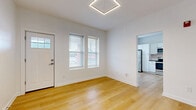 Located at 718 E Linwood Blvd in Kansas City, Missouri, this thoughtfully designed one-bedroom, one-bathroom unit offers a clean, modern aesthetic across a well-utilized single floor. Light-toned hardwood-style flooring runs consistently throughout the space, complementing the crisp white walls and creating a bright, cohesive feel.

The open living area welcomes natural light through multiple windows fitted with blinds, and features a striking geometric hexagonal pendant light fixture overhead. The kitchen is well-appointed with white shaker-style cabinetry, dark countertops, a white subway tile backsplash, and a full suite of stainless steel appliances including a refrigerator, range, microwave, and dishwasher. A dedicated laundry area with a stacked washer and dryer unit adds convenient in-unit functionality.

The bedroom is a comfortable, well-proportioned room with continued hardwood-style flooring, dual windows for natural light, and access to a closet. The bathroom is finished with a mosaic tile floor, large-format stone-look wall tiles surrounding the tub and shower, and a modern wood-toned vanity with brushed hardware. A small window provides ventilation and additional natural light. The overall ambiance is clean, contemporary, and move-in ready.