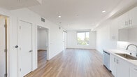 This well-appointed upper-floor unit presents a clean, contemporary design throughout its thoughtfully arranged layout. The open-concept living and kitchen area serves as the heart of the space, featuring crisp white cabinetry, stainless steel appliances including a dishwasher, range, microwave, and refrigerator, and light quartz countertops. Recessed lighting illuminates the kitchen and flows seamlessly into the living area, which is anchored by warm hardwood-style flooring that extends throughout the entire unit.

Large windows in the main living area frame views of the surrounding neighborhood and greenery, filling the space with abundant natural light. A sliding glass door provides access to an outdoor balcony area, further enhancing the sense of openness.

The bedroom features a generously sized sliding-door closet with built-in shelving, offering practical storage solutions. An additional room benefits from its own window with elevated outdoor views. The bathroom is finished with elegant large-format marble-style tile in the tub surround, complemented by a sleek vanity with dark wood cabinetry, a soaking tub with shower, and consistent hardwood-style flooring. White walls and recessed lighting throughout contribute to the unit's bright, modern aesthetic.