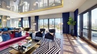 Located at 501 NW Seventh Ave in Fort Lauderdale, FL, this upscale amenity lounge delivers a striking blend of contemporary design and resort-style comfort across a generously proportioned single floor. The interior is immediately distinguished by its dramatic high-gloss reflective ceiling framed with gold-lit cove lighting, creating a luminous, jewel-box ambiance throughout the main lounge. Floor-to-ceiling glass walls and sliding doors flood the space with abundant natural light while framing panoramic views of the Fort Lauderdale skyline and surrounding cityscape.

The main lounge area features bold, curated furnishings including a vibrant magenta velvet sofa, deep navy accent chairs, and a graphic black-and-white zebra-print area rug layered over an intricate parquet hardwood floor. A dedicated bar and social zone at the rear showcases a sleek counter lined with cobalt blue barstools, globe pendant lighting, a tiled accent wall, and a wall-mounted display screen — ideal for gatherings and events.

The space seamlessly transitions to two distinct outdoor terraces. One features a pergola-covered lounge with plush sectional seating and commanding skyline views, while the other offers alfresco dining tables bathed in South Florida sunshine. Together, these areas create a well-rounded environment suited for both relaxed socializing and curated events.