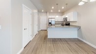 This single-floor residence offers a clean, modern aesthetic with a thoughtfully designed open-concept layout. The main living area is spacious and bright, featuring light wood-look flooring, recessed lighting, and a large sliding glass door fitted with vertical blinds that fills the space with natural light.

The kitchen is a standout feature, showcasing white shaker-style cabinetry, granite countertops, and a full suite of stainless steel appliances including a refrigerator with ice maker, electric range, microwave, and dishwasher. A peninsula with pendant lighting serves as a natural divider between the kitchen and living area, adding both function and style. Recessed lighting and an additional chandelier keep the space well-lit.

The bedrooms are carpeted for comfort and include ample natural light through blinds-covered windows. The primary bedroom connects directly to an en-suite bathroom featuring white cabinetry, granite countertops, and a large mirror. A second bathroom offers a full soaking tub and shower combination with built-in shelving, all finished in crisp white.

Throughout the unit, neutral warm-beige walls, white trim, and consistent flooring choices create a cohesive and inviting atmosphere well-suited for comfortable everyday living.