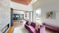 Located at 42 Broad St W in Mount Vernon, NY, this thoughtfully designed single-floor amenity space offers a generous, open layout that comfortably accommodates two distinct living areas. The interior showcases a bold contemporary aesthetic, with light hardwood flooring flowing throughout and carefully curated artwork adorning the walls.

The first lounge area serves as a vibrant social hub, featuring a striking built-in blue bench with a graphic patterned acoustic backdrop, complemented by plush blue armchairs and a round wood coffee table. Large windows flood the space with natural light and provide views of the surrounding streetscape. A glass pivot entry door adds a sleek architectural detail.

The second living zone caters to entertainment and relaxation, anchored by a deep blue accent wall beneath a textured wood-panel ceiling with recessed lighting. Built-in banquette seating with striped cushions faces a wall-mounted flat-screen TV, making it ideal for group gatherings. Nearby, a central billiards table beneath a modern circular pendant light serves as a standout recreational feature.

A bar area with mosaic tile backsplash, white counter stools, and elegant pendant lighting rounds out the space, while high-top dining tables with warm wood chairs provide additional seating. The overall ambiance is energetic yet refined, blending bold color choices with modern furnishings throughout.