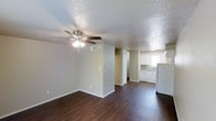 This two-floor space offers a practical and functional layout designed for comfortable everyday living. The main living area features rich, dark hardwood-style flooring that contrasts beautifully with the light neutral-toned walls, creating a warm yet understated aesthetic throughout. A ceiling fan with an integrated light fixture is centrally positioned, providing both air circulation and ambient lighting. The textured ceiling adds a classic touch to the interior design.

The living area flows seamlessly into the kitchen, which is outfitted with white cabinetry, a white refrigerator, and a white dishwasher or range, giving the space a clean and cohesive look. A window above the kitchen sink allows natural light to filter in, brightening the workspace. The open-concept design between the living and kitchen areas enhances the sense of spaciousness and encourages easy movement throughout the main level.

A hallway visible from the living area leads to additional rooms, suggesting a well-organized floor plan that separates the living and private spaces. The neutral color palette used throughout creates a versatile backdrop, making it easy to personalize with furnishings and décor. Overall, this two-floor space balances simplicity and functionality, making it well-suited for a variety of lifestyles.