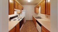 This single-floor unit presents a practical and well-organized layout designed for comfortable everyday living. The entryway welcomes residents with tile flooring and a large sliding closet, providing convenient storage from the moment you step inside. A hallway connects the main areas, maintaining a logical flow throughout the space.

The living area is generously proportioned, finished with neutral carpet and bright white walls. Multiple windows line the far wall, allowing natural light to fill the room, while a wall-mounted air conditioning unit and baseboard heating ensure year-round comfort. The open feel of this space makes it well-suited for a variety of furniture arrangements.

The galley-style kitchen runs along two parallel walls, lined with warm oak cabinetry offering ample upper and lower storage. White appliances including a coil-top range, refrigerator, and dishwasher are in place, complemented by light countertops and a double-basin sink. Tile flooring adds durability in this high-use area.

Both bedrooms are carpeted and finished with the same neutral palette, each featuring wide windows that frame outdoor greenery and baseboard heating beneath. The full bathroom includes a tub-shower combination, a single-sink vanity with oak cabinetry, a large mirror, and tile flooring, completing the unit with clean, functional finishes.