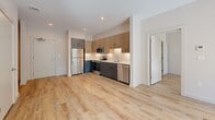 Located at 250 Water St in Williamstown, MA, this thoughtfully designed two-bedroom, two-bathroom residence offers a well-appointed single-floor layout with modern finishes throughout. Light wood-tone flooring flows seamlessly across the open-concept living and kitchen area, creating a bright and cohesive atmosphere. The kitchen is outfitted with two-tone cabinetry — warm wood uppers paired with dark lower cabinets — a subway tile backsplash, and a full suite of stainless steel appliances including a refrigerator, range, microwave, and dishwasher. The main living area opens directly to a private outdoor balcony through floor-to-ceiling black-framed glass doors, filling the space with natural light and tree-lined views. Both bedrooms feature the same warm wood flooring, large black-framed windows overlooking lush greenery, and generous closet storage, including a walk-in closet with wire shelving in the primary bedroom. The two bathrooms are finished with dark slate-style floor tiles, warm wood vanities with quartz countertops, and spa-inspired walk-in showers clad in large-format terrazzo-style stone tile. A hallway connects all rooms efficiently, completing this clean, contemporary residence.