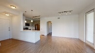 This single-floor residence is designed with an open-concept layout that seamlessly connects the kitchen and living areas. The kitchen serves as a central hub, featuring a large white island with a built-in sink, pendant lighting, and a suite of stainless steel appliances, including a range, over-the-range microwave, and refrigerator. Gray-toned cabinetry, a marble-style tile backsplash, and under-cabinet lighting complete the kitchen's polished aesthetic. Track lighting overhead extends into the living area, which is spacious and bright, with hardwood-style flooring running throughout the unit. An arched doorway adds an architectural detail, lending a classic touch to the otherwise modern interior.

The living area benefits from a row of windows that bring in natural light and views of the surrounding greenery. A ceiling fan with a light fixture is present in the bedroom, which also features access to a well-organized walk-in closet with built-in shelving and hanging rods. The bathroom includes both a soaking tub and a separate glass-door shower, accompanied by wood-look flooring consistent with the rest of the unit. Crown molding and clean white walls contribute to the cohesive, contemporary feel of the space throughout.