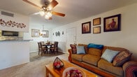 Located at 5421 Desoto Pkwy in Sarasota, Florida, this single-floor residence offers a comfortable and cohesive layout designed for everyday living. The living room serves as the heart of the home, featuring plush carpeting, a ceiling fan with integrated lighting, and a sliding glass door that opens to an outdoor view of lush greenery, filling the space with natural light. The dining area flows seamlessly from both the living room and kitchen, finished with wood-look flooring, a chandelier overhead, and wainscoting along the walls that adds a classic architectural touch. The kitchen is efficiently arranged with cream cabinetry, granite-style countertops, a mosaic tile backsplash, black appliances, and a pass-through peninsula connecting to the dining space. The bedroom is a restful retreat with carpeted floors, multiple windows with curtains, and direct access to a walk-in closet. The bathroom features a tub-shower combination with tiled surround and wood-look flooring. Textured ceilings are present throughout the home, contributing to its warm, residential character. The overall ambiance is inviting and practical, with a layout that maximizes functionality across each room.