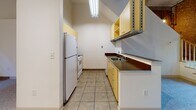 Located at 51 Front St in Lincoln, Rhode Island, this two-floor unit is housed within a historic mill building that masterfully combines industrial heritage with comfortable living. The space immediately distinguishes itself through its exposed brick walls, oversized multi-pane windows, and visible structural beams on the upper level — hallmarks of classic New England mill architecture that lend the unit a distinctive, character-rich ambiance.

The carpeted living areas across both floors offer a quiet, soft contrast to the building's industrial bones. Large arched windows frame views of the surrounding brick architecture, allowing natural light to fill the rooms throughout the day. Upper-level rooms feature exposed ceiling beams that reinforce the historic character of the structure.

The galley-style kitchen is efficiently designed, featuring yellow cabinetry, dark countertops, tile flooring, and a full suite of white appliances including a refrigerator, range, microwave, and dishwasher. Overhead fluorescent lighting ensures a bright and practical workspace.

The bathroom is well-appointed with warm-toned tile flooring, a vanity with granite-style countertops and yellow cabinetry, a tub-shower combination with white tile surround, and a multi-light chandelier fixture overhead. A louvered closet door adds a classic touch to the space.

Overall, this unit offers a compelling mix of historic architectural detail and practical, updated amenities in a storied Lincoln mill setting.