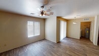 This single-story residence offers a practical and comfortable layout designed for everyday living. The open living area is finished with wood-look flooring and features a ceiling fan with light fixture, a large window dressed with horizontal blinds that allows ample natural light, and a sliding glass door with vertical blinds providing access to the exterior. A pendant light fixture illuminates an adjacent dining area, lending subtle definition between the two spaces.

The kitchen is well-equipped with warm-toned wood cabinetry extending to the ceiling for generous storage, dark laminate countertops, a double-basin stainless steel sink, a white electric range with coil burners, an over-the-range microwave, a refrigerator, and a dishwasher. Wood-look flooring continues seamlessly throughout.

The bedrooms are comfortably sized, each featuring ceiling fans, wood-look flooring, and open walk-in closets with built-in shelving for organized storage. The bathrooms include a tiled tub-shower combination unit and a separate bathroom with a vanity featuring wood cabinetry and dark countertops. A dedicated laundry room accommodates a full-size washer and dryer and includes an overhead storage shelf and a small window for ventilation.