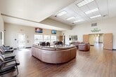 The Sablewood Gardens community clubhouse at 2600 Sablewood Dr in Bakersfield, California, is a well-appointed single-story amenity facility designed to serve residents with a comprehensive range of shared spaces. Rich hardwood flooring runs throughout, lending warmth and continuity across every room.

The centerpiece of the facility is a generously sized great room with soaring vaulted ceilings and abundant overhead lighting. This open lounge area accommodates large curved leather sectional sofas, coffee tables, and wall-mounted televisions, creating a comfortable gathering environment. The space transitions naturally into a dining area furnished with dark wood tables and chairs, also equipped with wall-mounted screens and lined with windows that bring in natural light and views of the surrounding community.

Two fully equipped kitchens support the facility, each featuring dark cabinetry, granite countertops, hardwood flooring, and black appliances including full-size refrigerators — ideal for catering events or everyday resident use.

A dedicated fitness center offers a suite of modern cardio and strength equipment, including treadmills, ellipticals, and free weights, with mirrored walls and windows overlooking the exterior grounds. The entrance corridor, lined with glass partitions and branded signage, provides a clean and professional first impression. Hallways connect all areas efficiently, completing a thoughtfully organized and functional community space.