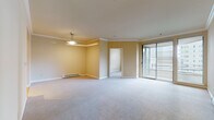 This single-floor residence offers a thoughtfully designed layout connecting multiple living spaces through a hardwood-floored corridor. The entry hallway features a built-in closet with a hanging rod, providing immediate storage upon arrival. The corridor leads naturally toward the main living areas, where natural light filters in from large windows at the end of the hall.

The spacious living room is finished with plush neutral carpeting and warm beige walls accented by elegant crown molding. A pendant light fixture adds a refined touch, while a large sliding glass door with horizontal blinds opens to an outdoor balcony, allowing abundant natural light and views of the surrounding urban landscape. A baseboard heating system runs along the perimeter walls throughout the carpeted areas.

The kitchen is efficiently designed with rich wood cabinetry, dark granite countertops, a tile backsplash, and a full suite of stainless steel appliances including a refrigerator, range, microwave, and dishwasher. Track lighting above adds practical illumination to the workspace, and light hardwood flooring completes the look.

The bedrooms are carpeted and generously proportioned, each benefiting from windows with urban views. The bathroom features a soaking tub with floor-to-ceiling white tile surround, accented by a vertical mosaic tile strip, complemented by hardwood flooring and clean, modern fixtures.