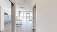 This thoughtfully designed studio offers a bright, modern living experience within a compact footprint. The open-concept main living area is anchored by dramatic floor-to-ceiling windows that frame sweeping outdoor views and flood the space with natural light. A ceiling fan overhead adds both function and style, while light-toned hardwood flooring runs throughout, lending warmth and visual continuity. A wall-integrated murphy bed with built-in cabinetry maximizes the versatility of the living space, and a sleek multi-functional table serves as both a dining and workspace solution.

The kitchen is a standout feature, showcasing a contemporary design with wood-grain lower cabinetry, frosted glass upper cabinets, a soft blue subway tile backsplash, and white quartz countertops. Stainless steel appliances — including a refrigerator and built-in dishwasher — along with a smooth cooktop and range hood complete the setup. The bathroom is finished in clean, neutral tones with large-format floor tiles, a full soaking tub with overhead shower, a mirrored vanity, and white wall tiles. The balcony provides outdoor access and enhances the sense of openness throughout the unit. Overall, the space exudes a clean, minimalist aesthetic with smart, functional design details throughout.