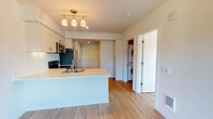 This single-floor unit is designed with a clean, modern aesthetic and an efficient, open layout. The kitchen serves as a central feature, equipped with a full suite of stainless steel appliances including a refrigerator, electric range, and over-the-range microwave. White flat-panel cabinetry extends to the ceiling, maximizing storage, while light-toned countertops and a tiled backsplash provide a crisp, contemporary finish. A peninsula with an integrated sink and pendant track lighting above adds both functionality and visual interest, seamlessly connecting the kitchen to the living area. Light wood-look flooring runs throughout the main living spaces, contributing to the unit's bright and cohesive feel. A dedicated laundry closet houses a stacked washer and dryer, offering convenient in-unit functionality. The bedroom is a comfortable, well-proportioned space featuring the same wood-look flooring, a ceiling fan with light fixture, and a large window that frames views of surrounding greenery, filling the room with natural light. The bathroom includes a full soaking tub with shower combination, chrome fixtures, and a wall-mounted storage cabinet, maintaining the unit's clean and practical design throughout.