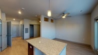 This studio is thoughtfully designed to maximize functionality within a single-floor, open-concept layout. The kitchen serves as a central focal point, showcasing dark espresso cabinetry that contrasts elegantly with light granite countertops on both the perimeter surfaces and a freestanding island. Stainless steel appliances, including a refrigerator, range, microwave, and dishwasher, complement the modern aesthetic, while a white tile backsplash adds a clean, polished finish. A pendant light above the island provides targeted task lighting, enhancing the kitchen's visual appeal.

The living area flows seamlessly from the kitchen, featuring light wood-style flooring that runs throughout the space, creating a cohesive and airy feel. A ceiling fan overhead adds both comfort and practicality. Architectural cutouts near the upper wall add a distinctive design detail, while a door leads to a walk-in closet, providing ample storage. Natural light enters through windows with blinds, and a set of double doors opens to an outdoor area.

The bathroom is efficiently arranged with dark cabinetry, a granite-topped vanity, an overhead cabinet for storage, and a full tub-shower combination with clean white tile surround.