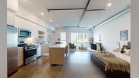 Located in the Mar Vista neighborhood of Los Angeles, this single-story loft-style unit at 4091 Redwood Ave offers a thoughtfully designed open-plan layout that seamlessly connects the kitchen, dining, and living areas. Polished concrete floors run throughout the main living space, complementing the industrial-modern aesthetic established by exposed metal ductwork and black track lighting overhead.

The kitchen is well-appointed with stainless steel appliances, including a gas range, built-in microwave, and French door refrigerator. Light wood cabinetry pairs with white upper cabinets and open shelving, while a textured mosaic tile backsplash adds visual interest. A freestanding island on casters provides flexible prep space and casual seating.

The living area is bright and open, anchored by a large sliding glass door that invites abundant natural light and leads to a private outdoor patio. A dedicated dining nook features windows on two sides, enhancing the airy feel of the space.

The bathroom is finished with a floating wood-grain vanity, white quartz countertop, and a large wall mirror, reflecting a clean, contemporary aesthetic.

Throughout the unit, the interplay of white walls, natural wood tones, and industrial accents creates a cohesive, modern atmosphere well-suited to urban Los Angeles living.
