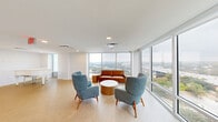 Located in Austin's vibrant 78702 zip code, this elevated sky lounge offers a refined communal gathering space defined by sweeping floor-to-ceiling windows that frame breathtaking panoramic views of the Austin skyline, Lady Bird Lake, and surrounding cityscape. The open, single-floor layout is bathed in abundant natural light, creating a bright and airy atmosphere throughout.

The living area serves as the centerpiece of the space, thoughtfully furnished with a cognac leather sofa and mid-century modern accent chairs in teal and gray upholstery, arranged around a round wood coffee table. Multiple seating vignettes are positioned to take full advantage of the wraparound views, making the area ideal for both relaxed gatherings and quiet contemplation.

The dining area features round tables paired with wood-framed chairs with blue upholstered seats, set against a backdrop of floor-to-ceiling windows overlooking the city. A separate seating alcove includes rich walnut built-in cabinetry, adding warmth and a refined finishing touch.

A kitchenette with warm wood cabinetry and tiled backsplash provides functional support for the space. A white grand piano tucked near the windows adds an elegant, artistic accent. Light wood-toned flooring flows consistently throughout, tying together the clean, contemporary design. The overall ambiance is polished, welcoming, and distinctly Austin.