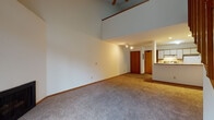 Located at 1210 McKenna Blvd in Madison, Wisconsin, this two-story residence offers a well-designed layout with a range of notable architectural features. The main level centers around a generously proportioned living area distinguished by dramatic vaulted ceilings that rise to impressive heights, creating a sense of openness and grandeur. A ceiling fan complements the space, while plush carpeting runs throughout the main living areas. A fireplace anchors one end of the living room, and sliding glass doors provide access to an outdoor balcony, inviting natural light into the space. The kitchen is efficiently laid out in a galley style, featuring white cabinetry, laminate countertops, a full suite of appliances including a range, refrigerator, and dishwasher, and tile flooring. A breakfast bar separates the kitchen from the living area, adding functionality. A full bathroom on the main level includes a tub-shower combination and tile flooring. A wood-railed staircase leads to the upper level, where a spacious loft overlooks the main floor below. This upper space benefits from a skylight that floods the area with natural light, vaulted ceilings, and carpeted flooring, making it a versatile and bright additional living area.