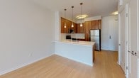 Located on the fourth floor of 1980 Kettner in San Diego, this well-appointed unit showcases a thoughtfully designed single-floor layout with a clean, contemporary aesthetic throughout. The open-concept kitchen serves as the heart of the space, featuring warm walnut-toned cabinetry that extends to the ceiling for ample storage, a white quartz peninsula with an undermount sink, and a full suite of stainless steel appliances including a gas range, built-in microwave, dishwasher, and refrigerator. A white subway tile backsplash and stylish pendant lighting add modern character to the space. Light hardwood-style flooring flows through the kitchen and living areas, creating a seamless, airy feel. The bedroom is generously proportioned, bathed in natural light from a large sliding window that frames views of the surrounding neighborhood. Plush wall-to-wall carpeting and a ceiling light fixture complete this comfortable retreat. The bathroom is finished with a clean, minimalist design, featuring floor-to-ceiling white tile surrounding a soaking tub and rain showerhead, dark slate-toned floor tiles, a wood-accented storage cabinet, and a streamlined vanity. Together, these spaces offer a polished, functional living environment in one of San Diego's most desirable urban neighborhoods.