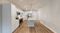 This single-floor residence in Greensboro, NC offers a thoughtfully designed layout with a seamless blend of modern finishes and functional living spaces. The kitchen serves as a standout centerpiece, showcasing white shaker-style cabinetry, a classic subway tile backsplash, light-toned granite countertops, a large center island with pendant lighting, and a full suite of stainless steel appliances. Rich hardwood-style flooring flows throughout the main living and kitchen areas, lending warmth and continuity to the open floor plan. The living area benefits from natural light through large windows and features direct outdoor access via a glass-panel door. The bedrooms are finished with plush carpeting, ceiling fans, and generous windows with exterior views. One bedroom includes built-in shelving, adding practical storage and character. The bathroom is elegantly appointed with a dual-sink vanity topped with marble-style counters, a large mirror, tile flooring, and a full tub-shower combination. Clean white walls and consistent trim work throughout the space create a bright, cohesive aesthetic well-suited for comfortable everyday living.