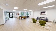 Located at 900 Farmington Ave in West Hartford, Connecticut, this thoughtfully designed amenity space offers a versatile and stylish environment across a single floor. Light hardwood flooring and a clean white drop-tile ceiling with recessed panel lighting run throughout, creating a bright, cohesive aesthetic.

The main lounge area is generously proportioned and filled with natural light from large floor-to-ceiling windows overlooking the surrounding neighborhood. It features a comfortable seating arrangement with a gray sofa, green velvet accent chairs, and a curated area rug, alongside wall-mounted artwork. A large-screen TV is mounted on the wall, making this area ideal for relaxing or casual gatherings. Plush white boucle lounge chairs and a second seating vignette add to the social atmosphere, complemented by a shuffleboard table for recreation.

A dedicated conference room provides a professional setting with a long light wood table, ergonomic rolling chairs, a wall-mounted display screen, and built-in power access — well-suited for meetings or presentations. An adjacent row of green stackable chairs offers additional flexible seating.

The kitchenette features white cabinetry, a stainless steel refrigerator, microwave, and a blue tile backsplash, providing practical support for gatherings. Together, these spaces form a well-rounded, modern communal environment.