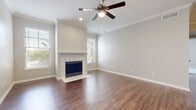 This single-floor home offers a thoughtfully designed layout that balances comfort and functionality throughout its living spaces. The main living area is a standout, showcasing rich hardwood-style flooring, elegant crown molding, and a classic tile-surround fireplace with a clean white mantel that serves as the room's focal point. A ceiling fan with integrated lighting keeps the space comfortable, while multiple windows fitted with blinds flood the room with natural light and offer views of lush greenery outside. The open layout flows seamlessly toward the kitchen area, which features a breakfast bar peninsula, gray shaker-style cabinetry, white subway tile backsplash, light countertops, and a full suite of white appliances including a refrigerator, range, microwave, and dishwasher — all set atop matching hardwood-style flooring. The bedrooms are finished with plush neutral carpeting and ceiling fans, providing a soft and restful atmosphere. One bedroom offers access to an outdoor space through sliding glass doors with vertical blinds, while another benefits from a large window framing peaceful outdoor views. The bathroom includes a soaking tub and shower combination with tile surround, complemented by hardwood-style flooring for a cohesive look throughout the home.