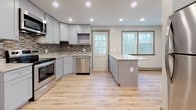 Located at 360 Daleville in Willington, this thoughtfully updated unit spans three floors and blends modern finishes with comfortable, functional design throughout. The kitchen stands as a true centerpiece, showcasing soft gray shaker-style cabinetry, stainless steel appliances, a mosaic tile backsplash, and a generous island wrapped in reclaimed wood-style paneling topped with a stunning granite countertop. Recessed lighting and a glass-paned exterior door invite abundant natural light into the space. Light-toned hardwood flooring flows seamlessly throughout the living areas and bedrooms, complemented by warm cream walls and crisp gray trim and baseboards. The bedrooms are bright and welcoming, each benefiting from multiple windows that frame views of the surrounding neighborhood and wooded scenery. Built-in closets provide practical storage solutions. The bathrooms are elegantly finished with large-format marble-style wall tiles, decorative mosaic border accents, and coordinating floor tile. One bathroom features a glass-enclosed shower with built-in niche shelving, while another includes a full soaking tub and shower combination with a window for ventilation. Together, these spaces create a clean, modern living environment with refined details at every turn.