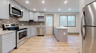 Located at 360 Daleville in Willington, this thoughtfully updated unit spans three floors and blends modern finishes with comfortable, functional design throughout. The kitchen stands as a true centerpiece, showcasing soft gray shaker-style cabinetry, stainless steel appliances, a mosaic tile backsplash, and a generous island wrapped in reclaimed wood-style paneling topped with a stunning granite countertop. Recessed lighting and a glass-paned exterior door invite abundant natural light into the space. Light-toned hardwood flooring flows seamlessly throughout the living areas and bedrooms, complemented by warm cream walls and crisp gray trim and baseboards. The bedrooms are bright and welcoming, each benefiting from multiple windows that frame views of the surrounding neighborhood and wooded scenery. Built-in closets provide practical storage solutions. The bathrooms are elegantly finished with large-format marble-style wall tiles, decorative mosaic border accents, and coordinating floor tile. One bathroom features a glass-enclosed shower with built-in niche shelving, while another includes a full soaking tub and shower combination with a window for ventilation. Together, these spaces create a clean, modern living environment with refined details at every turn.
