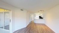 This well-appointed single-floor residence offers a clean, modern aesthetic throughout. The open-concept living and dining area is finished with warm hardwood-style flooring and crisp white walls, creating a bright and airy atmosphere. Large sliding glass doors lead to a private balcony with lattice railing, flooding the living space with natural light and offering pleasant views of surrounding greenery.

The kitchen is thoughtfully designed with white shaker cabinetry, light stone countertops, a decorative tile backsplash, and a full suite of stainless steel appliances including a refrigerator, electric range, and built-in microwave. A peninsula counter connects the kitchen to the living area, making it ideal for casual dining or entertaining. Track lighting above enhances the functional layout.

The bathroom features a full tub and shower combination with white tile surround, chrome fixtures, and a safety grab bar. A separate vanity area includes a wide white cabinet with an undermount sink, large mirror, and stylish lighting, offering generous storage and counter space. Closet space is conveniently accessible from the hallway. Throughout the unit, a neutral color palette and consistent finishes create a cohesive, move-in-ready environment.
